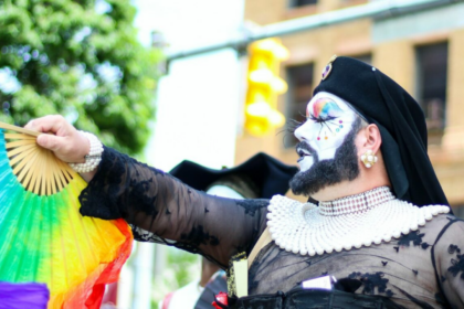 Persona caracterizada con barba portando un abanico con los colores de la bandera gay